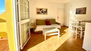 A room with a bed, a table, a chair, a painting, and a door. - Beachfront apartment with large terrace (Tarifa)