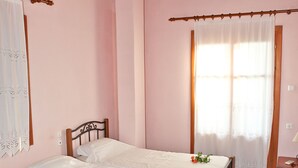 A room with two beds, wooden flooring, a wooden ceiling, and a window with curtains.