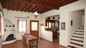 A spacious dining area with a wooden table and chairs, a fireplace, and a kitchen in the background.
