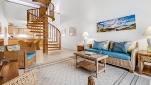 Un vaste espace de vie agrémenté d’un escalier en colimaçon en bois, de meubles en osier et d’un grand tableau représentant un paysage.