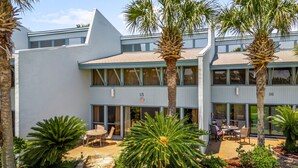A modern building with a flat roof, large windows, and a courtyard with palm trees and outdoor seating. - Unit 15, Pet Friendly 3 Bedroom Beach Condo (Panama City Beach)