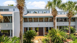 A two-story building with a flat roof, numbered 15 and 16, surrounded by palm trees and other tropical plants. - Unit 15, Pet Friendly 3 Bedroom Beach Condo (Panama City Beach)