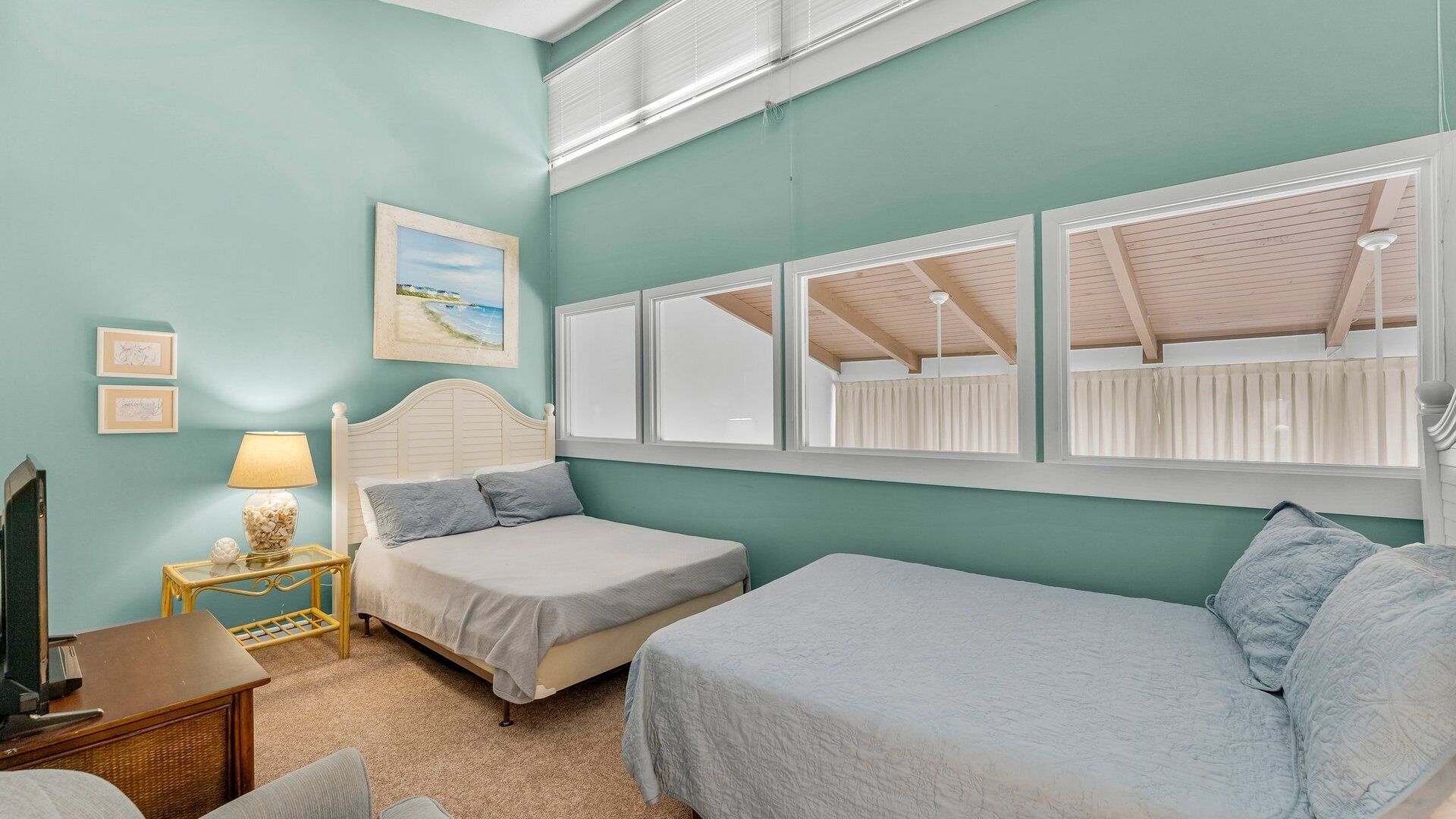 A bedroom with two beds, a nightstand with a lamp, a framed picture on the wall, and a window with blinds.