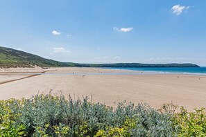 Une plage avec une vaste étendue de sable, un ciel bleu dégagé et des collines qui se dessinent à l’horizon.