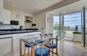 A modern kitchen with a dining area, a view of the outdoors, and a balcony. - 2 Bed in Ilfracombe (oc-bellev) (Ilfracombe)
