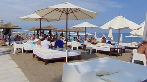 Um hotel à beira-mar com espreguiçadeiras e guarda-sóis, uma praia de areia e o mar ao fundo.