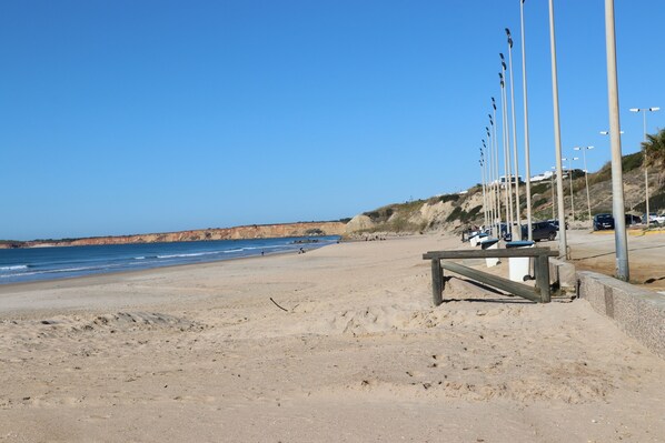 A sandy beach with a wooden bench and street lamps.