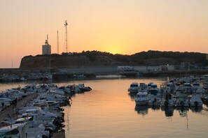 A marina with numerous boats docked, a prominent building with a tower, and a hilly landscape in the background.