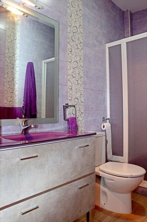 A bathroom with a large mirror, a purple towel, a white toilet, and a vanity with drawers. - Bright apartment close to beach (CONIL DE LA FRONTERA)