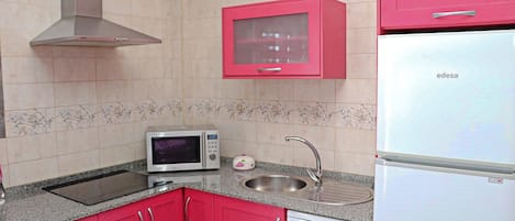 Una cocina con armarios rojos, microondas, fregadero y refrigerador blanco.