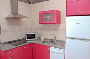 Eine Küche mit roten Schränken, einer Mikrowelle, einem Spülbecken und einem weißen Kühlschrank.