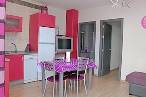 Een compacte keuken met een koelkast, magnetron en een klein eettafeltje met stoelen.