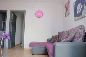 A living room with a grey sofa, a pink clock, and a door leading to another room. - Bright apartment close to beach (CONIL DE LA FRONTERA)