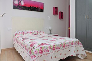 Une chambre à coucher avec un lit, une table de chevet, une lampe, une armoire et un tableau représentant un paysage urbain accroché au mur.