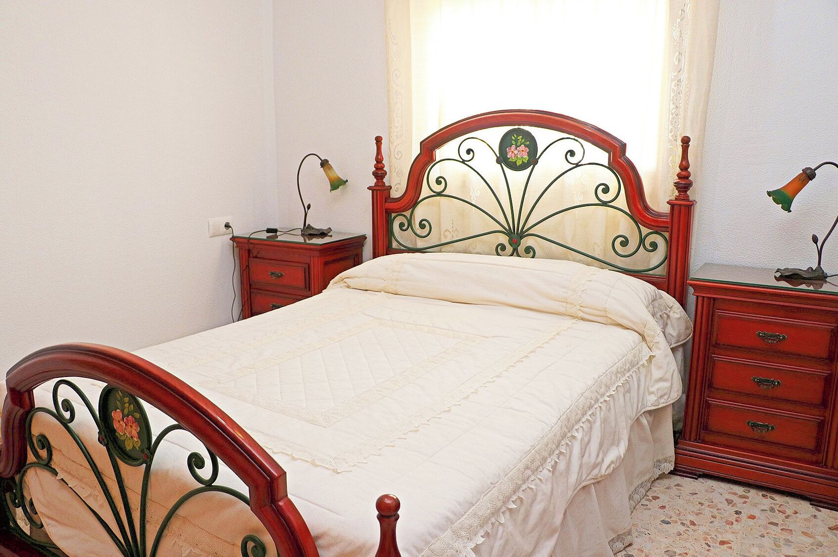 Um quarto com estrutura de cama de madeira, mesa de cabeceira com abajur e cômoda com gavetas.