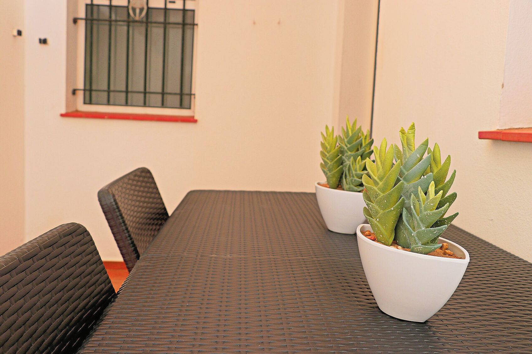 Een vergadertafel met twee potplanten, een zwarte geweven stoel en een raam met een metalen traliewerk.