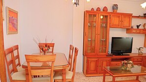 Un coin repas avec une table et des chaises en bois, un téléviseur posé sur un meuble en bois, et une table basse en verre sur laquelle se trouve un vase.