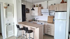 Een moderne keuken met een centraal eiland, barkrukken, een magnetron, een koelkast en houten keukenkastjes.