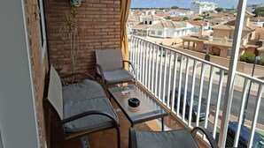 Een balkon met twee stoelen en een tafel, een bakstenen muur met decoratieve objecten, en uitzicht op een woonwijk.