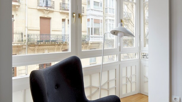 A room with a black chair, a white floor lamp, and a view of a building through a window. - Prim Suite by FeelFree Rentals (San Sebastián)