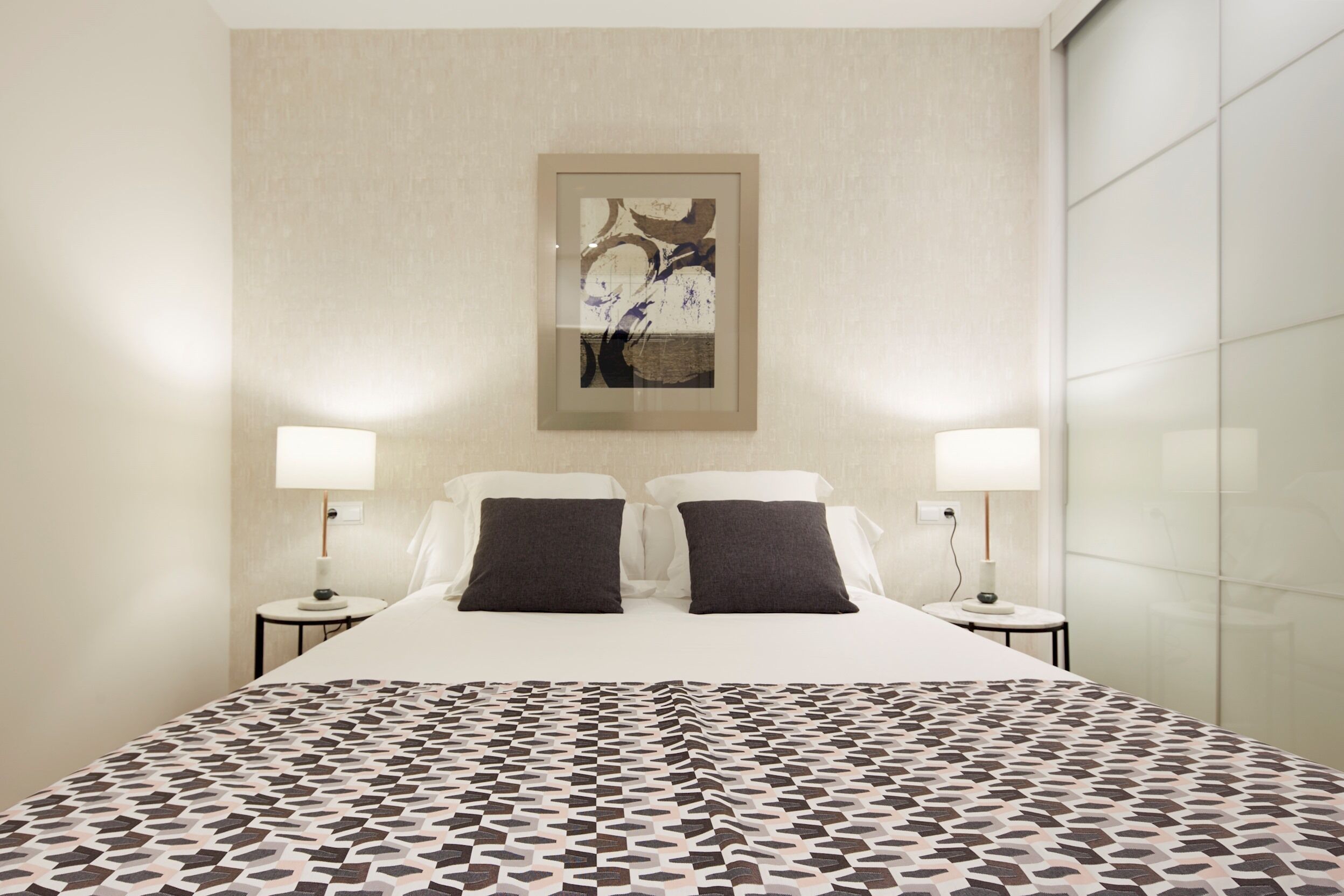 A hotel room with a large bed, two bedside tables, and a framed artwork on the wall.