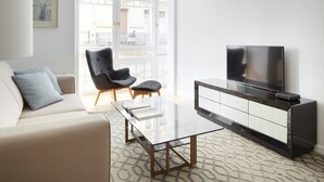 A modern living room with a sofa, armchair, glass coffee table, TV, and a view of the outside balcony. - Prim Suite by FeelFree Rentals (San Sebastián)