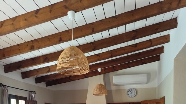 Ein gemütliches Wohnzimmer mit einer Couch, einem Esstisch und Stühlen. Im Hintergrund ist eine Küche mit Holzschränken und einem Herd zu sehen.