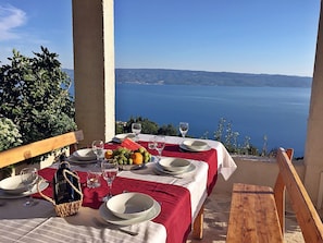 Une table dressée pour deux personnes, avec vue sur la mer, une bouteille de vin et un panier.