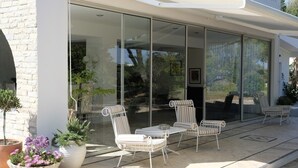 A modern house with a glass-enclosed patio area featuring outdoor furniture and potted plants. - Villa with 7 rooms, swimming pool, tennis court and garden (Alvor)