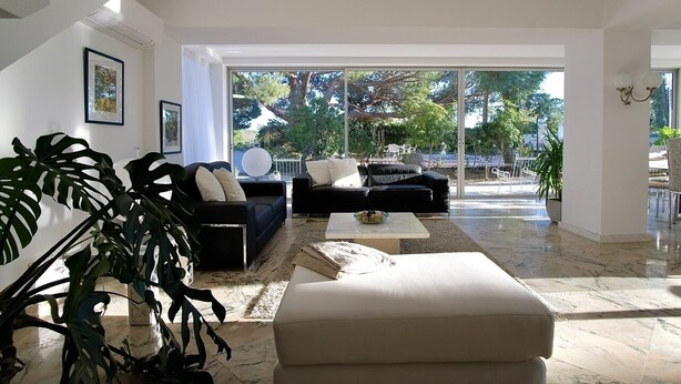 A spacious living room with a large window, a black sofa, a white armchair, and a coffee table. - Villa with 7 rooms, swimming pool, tennis court and garden (Alvor)