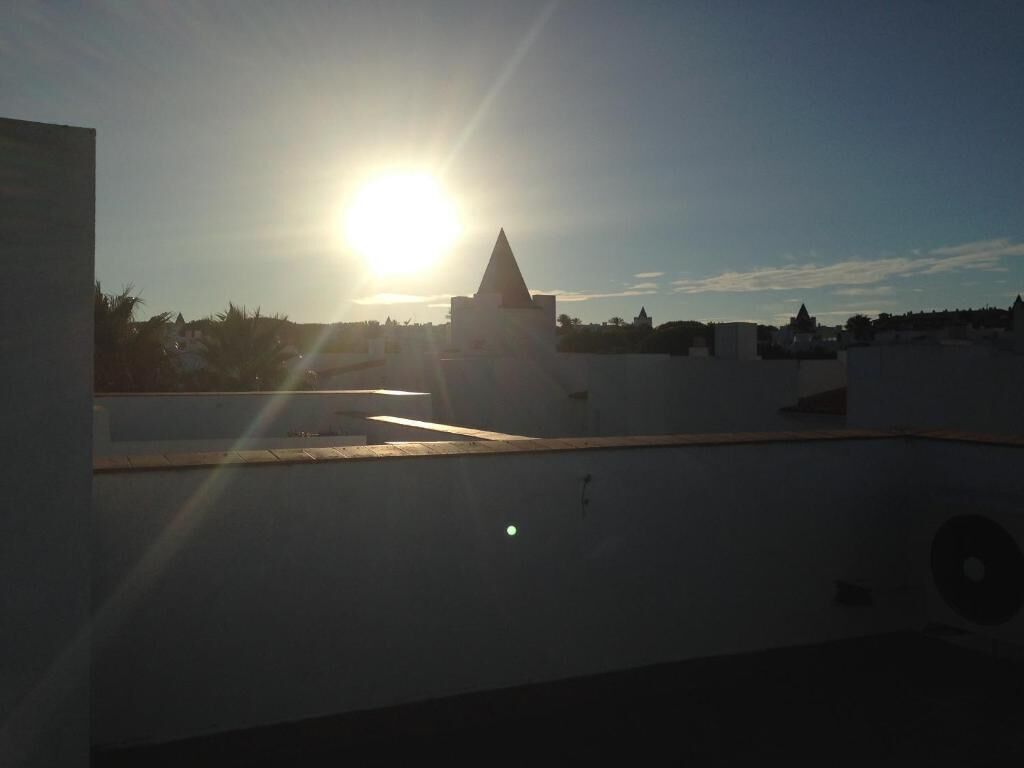 A rooftop with a view of a building with a pyramid-like structure in the distance, under a clear sky.
