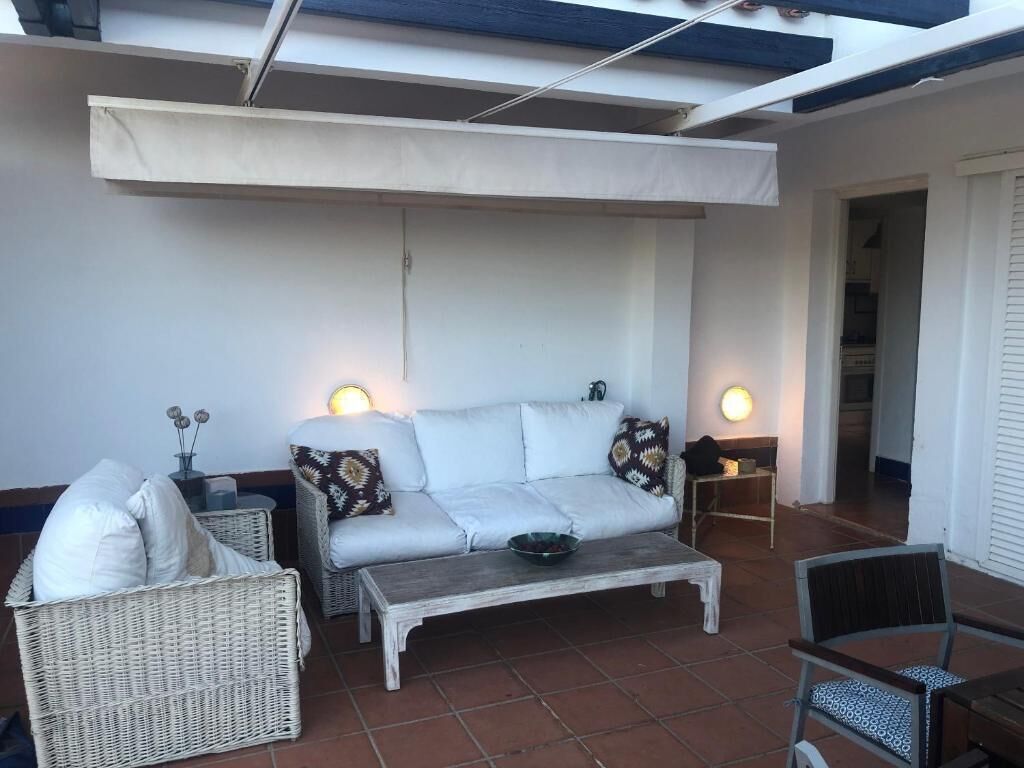 Ein gemütlicher Patio-Bereich mit einer weißen Couch, Korbstühlen und einem Couchtisch.
