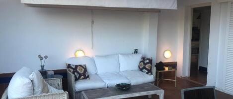 Ein gemütlicher Patio-Bereich mit einer weißen Couch, Korbstühlen und einem Couchtisch.