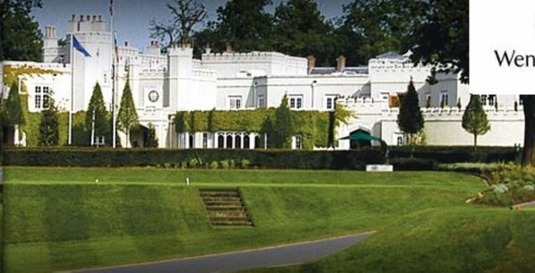 A large, white, castle-like building with a well-maintained lawn and a flagpole.