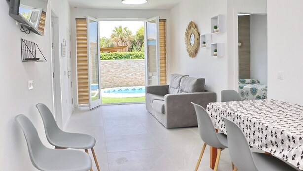 A modern living room with a grey sofa, a dining table with a patterned tablecloth, and a view of a swimming pool through open doors. - Lovely rural villa with private pool (CONIL DE LA FRONTERA)