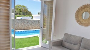 A room with a grey sofa, a large window with a view of a swimming pool, and a woven wall decoration. - Lovely rural villa with private pool (CONIL DE LA FRONTERA)