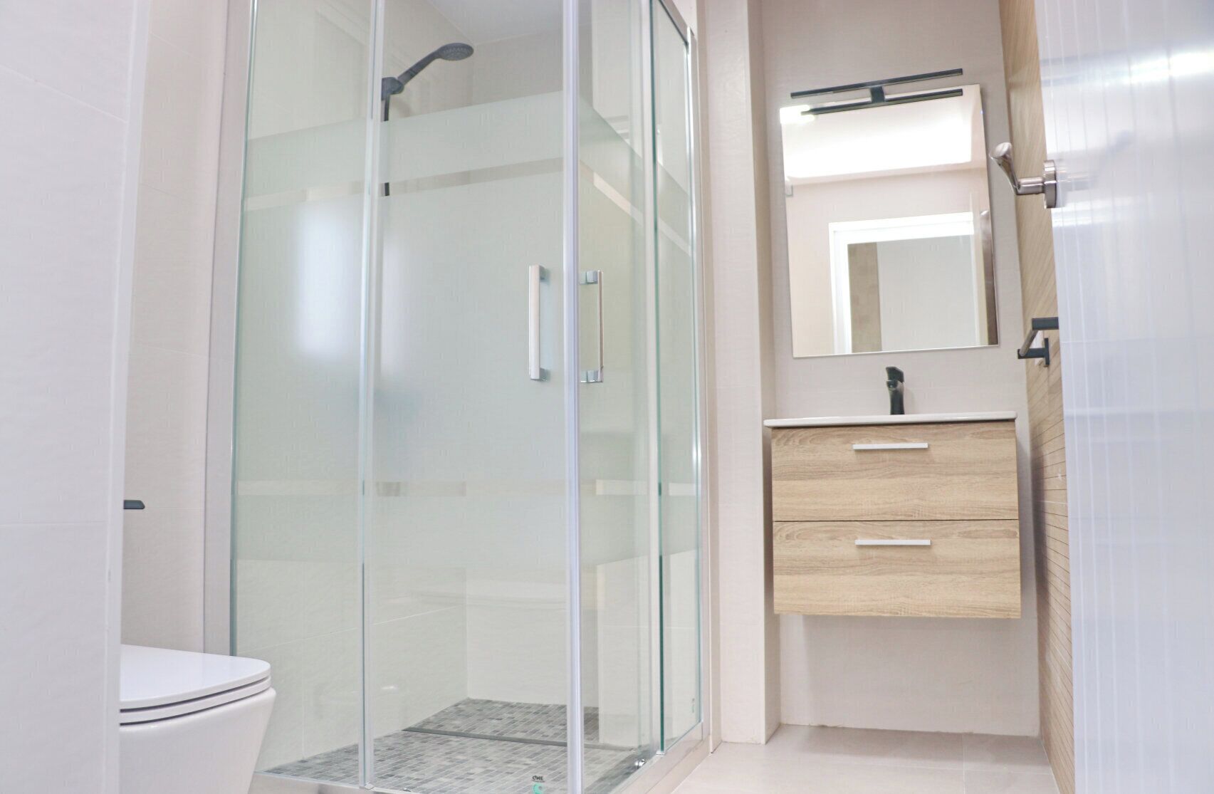 A modern bathroom with a glass-enclosed shower, a toilet, and a vanity with a mirror and drawers.
