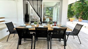 Uma sala de jantar com mesa posta para seis pessoas, rodeada por cadeiras pretas, sobre piso de madeira.