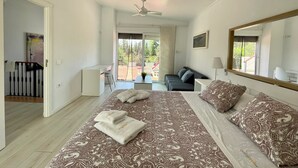 Quarto com cama grande, escrivaninha e varanda com mobiliário para exterior.