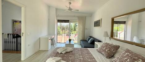 A bedroom with a large bed, a desk, and a balcony with outdoor furniture.