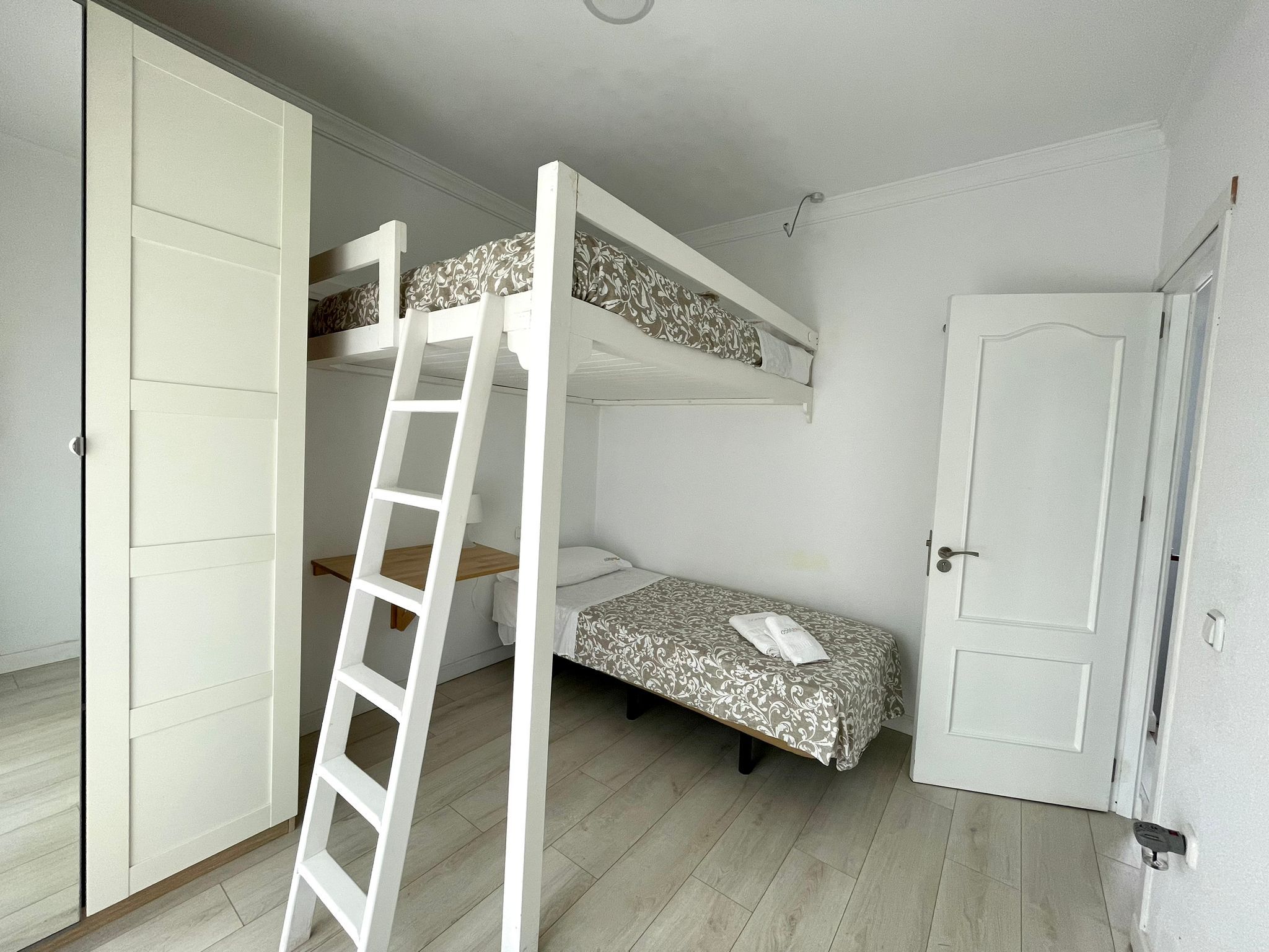 A room with bunk beds, a ladder, a door, and a small bedside table.