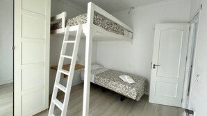 Quarto com beliches, escada, porta e uma pequena mesa de cabeceira.