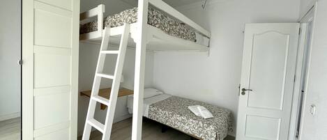 A room with bunk beds, a ladder, a door, and a small bedside table.