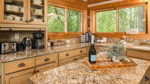 A kitchen with granite countertops, wooden cabinets, and large windows offering a view of trees. - Mountain Serenity! King Beds - Hot Tub - Fireplace - Ping Pong - Fire Pit (Boone)