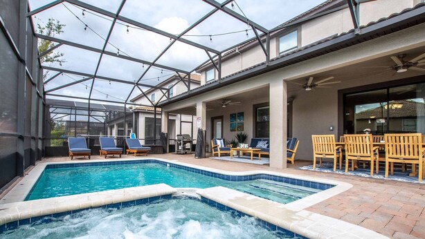 A swimming pool with a hot tub, lounge chairs, and a covered patio area. - Luxury Champions Gate Pool Home | Upgrades, Game Room, Spa & BBQ (Champions Gate)