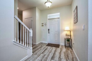 A hallway with a wooden floor, a white door, a staircase, and a wall-mounted sign that reads 'home.' - Luxury Champions Gate Pool Home | Upgrades, Game Room, Spa & BBQ (Champions Gate)