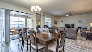 A spacious dining area with a wooden table and chairs, a chandelier, and a view through large sliding glass doors. - Luxury Champions Gate Pool Home | Upgrades, Game Room, Spa & BBQ (Champions Gate)
