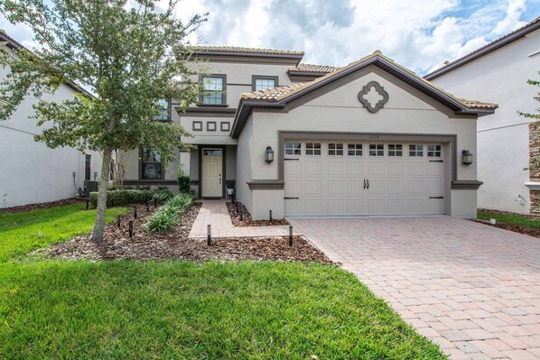 A two-story house with a garage, a landscaped front yard, and a brick driveway.