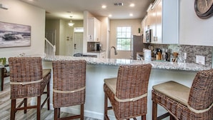 A kitchen with a central island, wicker bar chairs, and a clock on the wall. - Luxury Champions Gate Pool Home | Upgrades, Game Room, Spa & BBQ (Champions Gate)