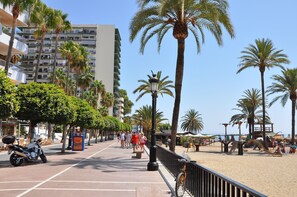 Une promenade en bord de mer bordée de palmiers, une plage et un immeuble doté de balcons.